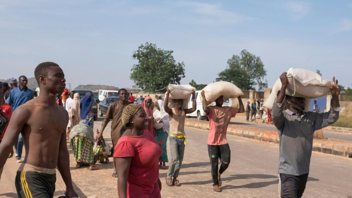 People carry bags of food on their heads during a mass looting of a warehouse that have Covid-19 food palliatives that were not given during lockdown to relieve people of hunger in Jos, Nigeria.