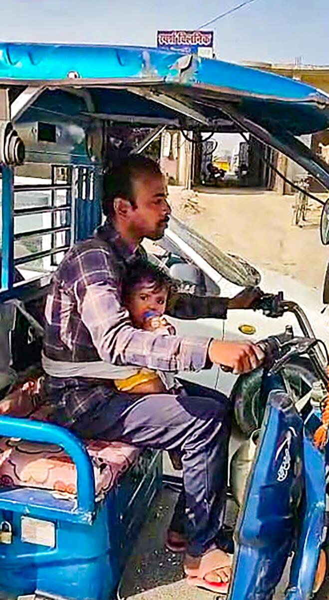 E-rickshaw driver Kamlesh Verma with his one year old daughter strapped to his body ferrying passengers in Ballia district on Saturday, April 22, 2023. — PTI