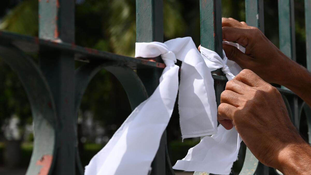 A man ties a white ribbon on a fence at a cemetery as a sign of protest against the government policy of forced cremations of Muslims who die of the coronavirus in Colombo.