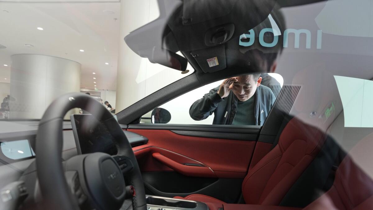 A man peeks at the interior of the Xiaomi SU7 electric car on display in Beijing. — AP