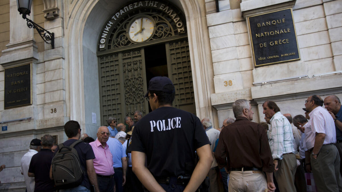 A police officer stands as pensioners wait outside the main gate of the national bank of Greece to withdraw a maximum of 120 euros ($134) in central Athens, Thursday, July 9, 2015. With a deadline just hours away to come up with a detailed economic reform plan, Greece requested a new three-year rescue from its European partners Wednesday as signs grew its economy was sliding toward free-fall without an urgently needed bailout. (AP Photo/Emilio Morenatti)