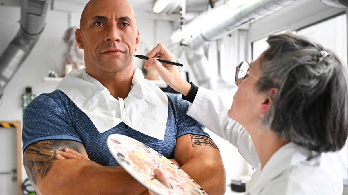 An employee adjusts the skin tone on the wax effigy of Dwayne Johnson, after the US actor complained about its pale skin tone, at the Grevin museum in Paris on October 24. — AFP