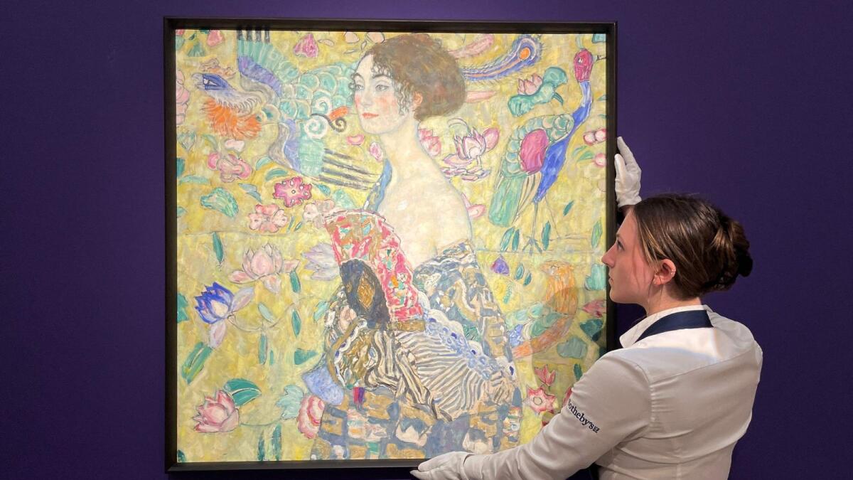 An employee poses with an artwork entitled 'Dame mit Facher (Lady with a Fan)' by Austrian artist Gustav Klimt, during a photocall at Sotheby's auction house in central London on June 20, 2023. — AFP