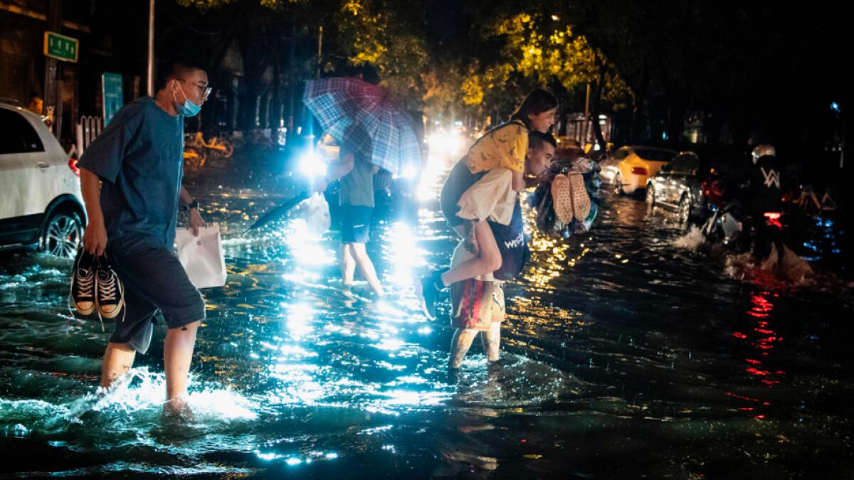 A man piggybacks a woman to cross a flooded street after sudden rain in Beijing on August 9, 2020. Photo: AFP