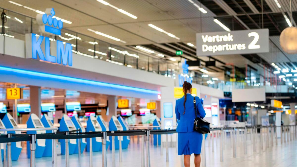 A KLM flight attendant walks in the Schiphol Airport, as Dutch airline KLM logo is seen. Dutch airline KLM said it will shed between 800 and 1,000 more jobs as the coronavirus pandemic is hitting the aviation sector for longer than expected.  — AFP