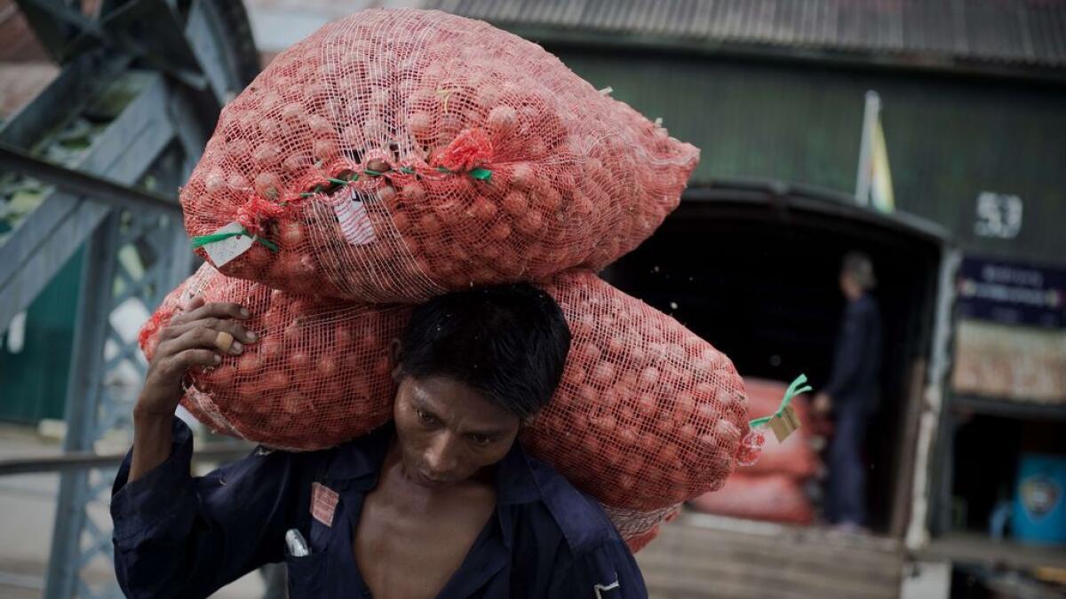 A worker carries bags of onions unloaded from a truck and onto a boat in Yangon on August 18, 2015. 