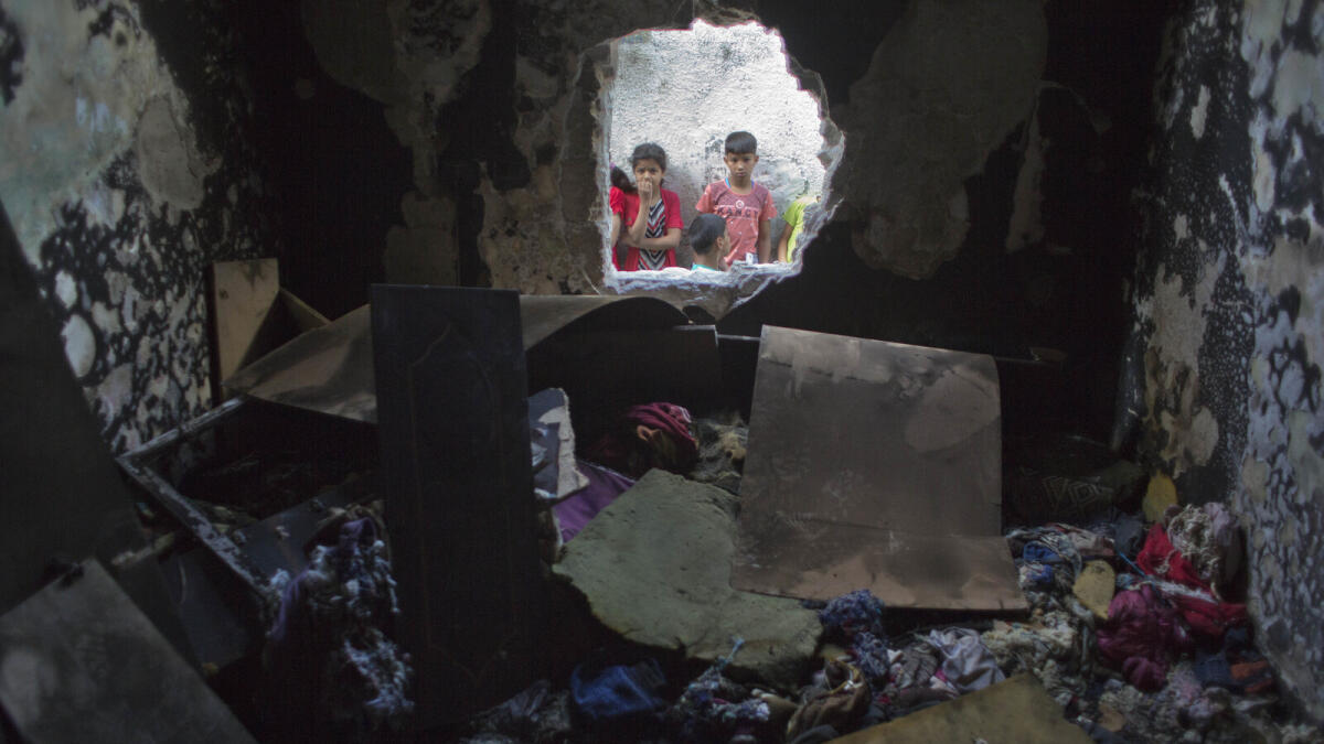 Palestinian children look through a hole in a wall at a burned bedroom where three children were killed by candle sparked on their family house in the Shati refugee camp in Gaza City, Saturday, May. 7, 2016.