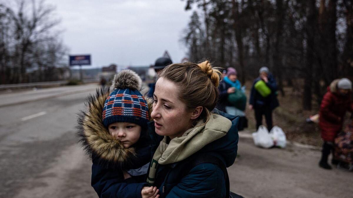 A woman carries her child as they flee the city of Irpin, northwest of Kyiv, on March 7, 2022. —AFP