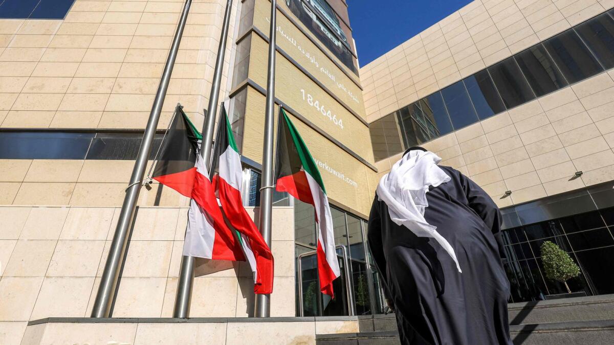 A man walks towards the entrance of a building past Kuwaiti national flags lowered to the half-mast position on December 16, as the Gulf country mourns the death of its leader Sheikh Nawaf Al Ahmad Al Sabah. — Photo: AFP