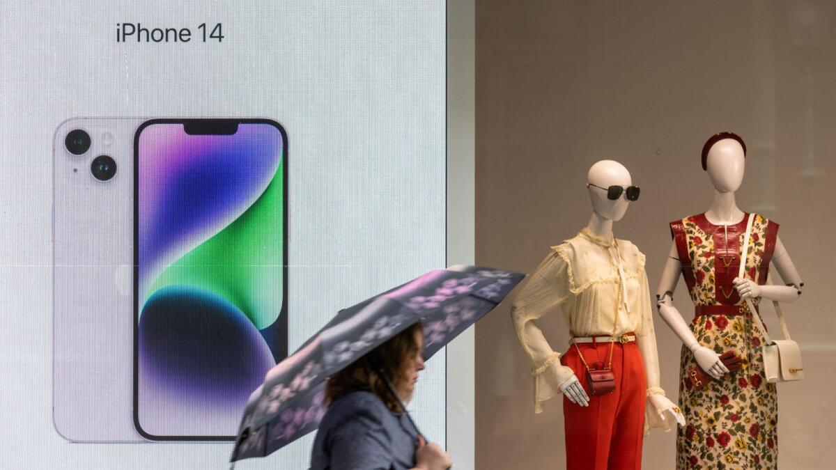 A woman with an umbrella walks past a display advertising Apple iPhone 14 during rainy weather in Moscow. — Reuters