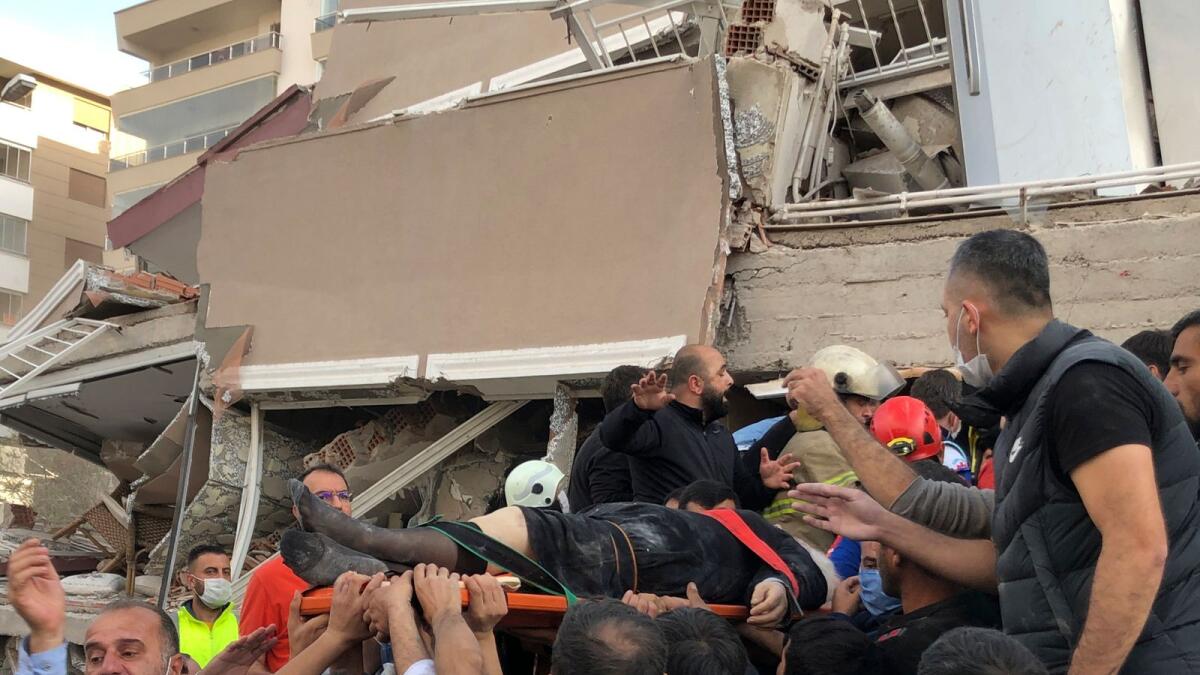 Rescue workers and local people carry a wounded person found in the debris of a collapsed building, in Izmir, Turkey. AP