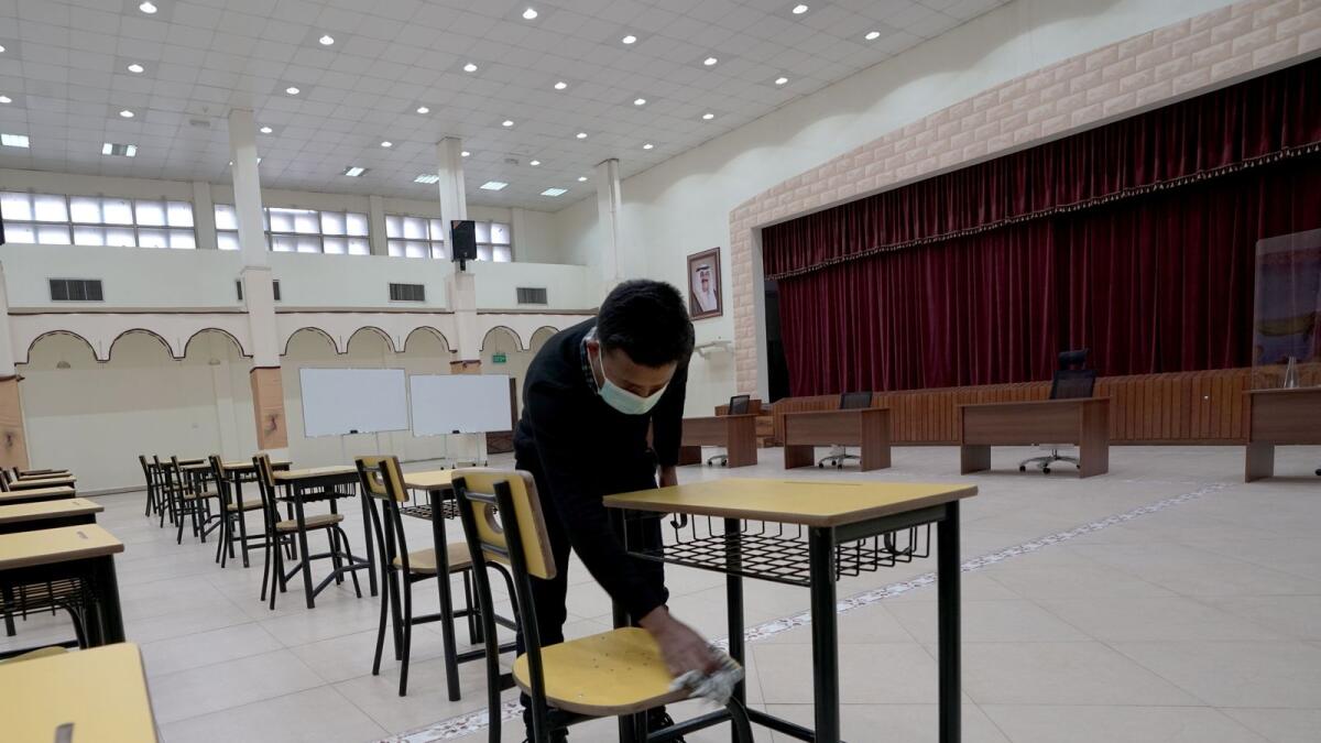 A worker cleans desks at a polling station ahead of parliamentary elections in Kuwait city. — Reuters