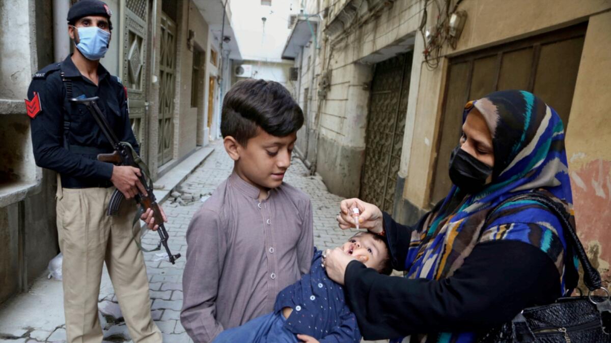 A Police officer stands guard while a health worker administers polio vaccine to a child in Peshawar. — AP