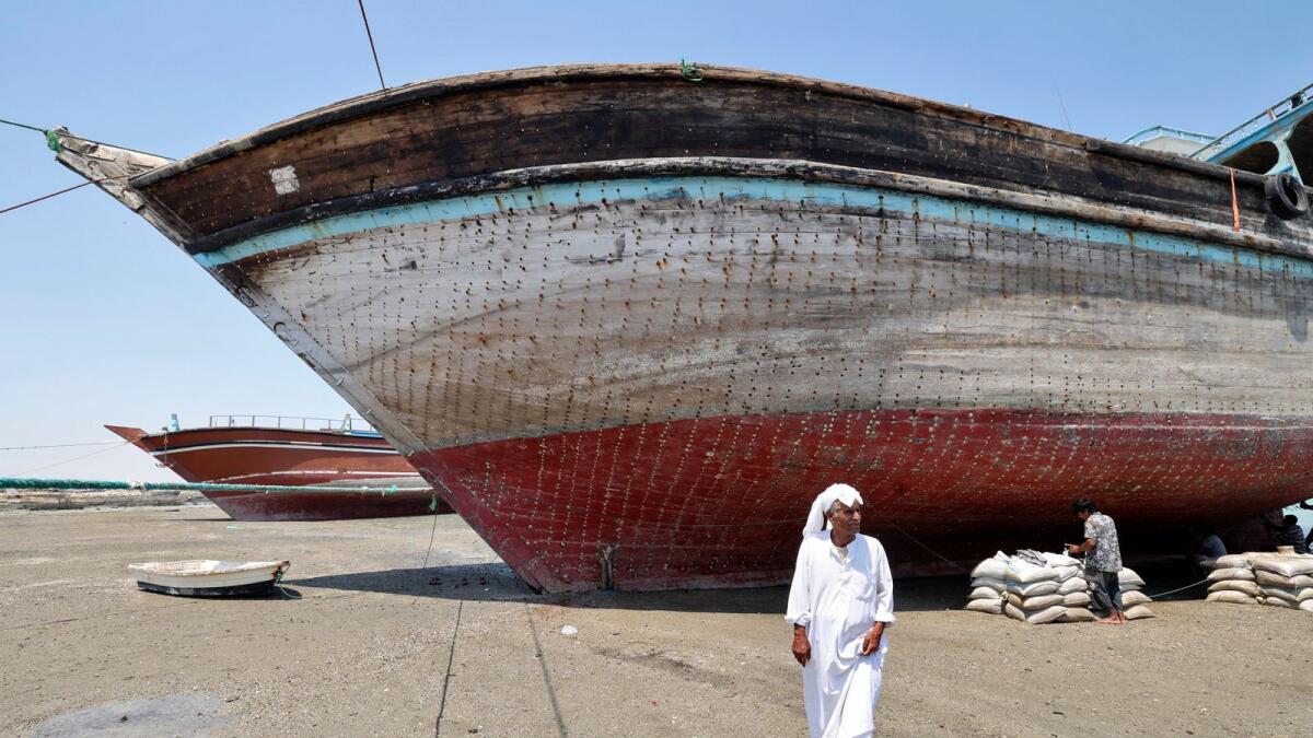 A man walks in front of a traditional wooden ships (lenj), laid ashore for restoration, in Iran's touristic Qeshm island in the Gulf, on April 29, 2023. — AFP