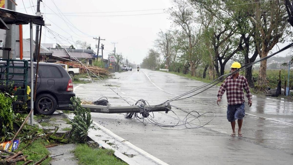 A resident walks on the highway amidst a toppled electric post after Typhoon Yutu slammed Isabela province in northeastern Philippines.-AP