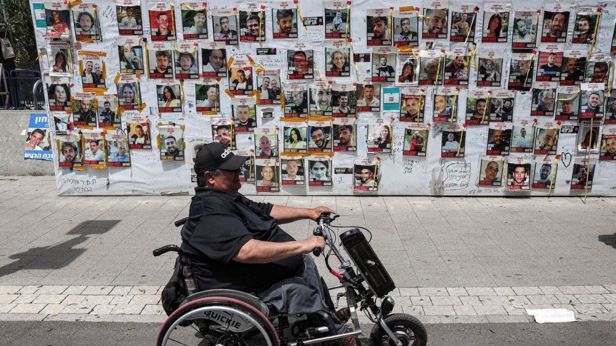 A person sitting in an electric wheelchair moves past posters of Israeli hostages held in Gaza since the October 7 attacks by Palestinian militants, during a protest by the families of the hostages and their supporters outside the Defence Ministry headquarters in Tel Aviv. — Photo: AFP