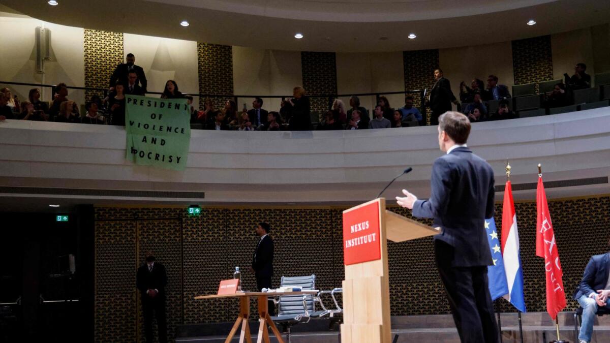 Students deploy a protest banner which reads 'President of violence and hypocrisy' during French President Emmanuel Macron's speech to the Nexus Institute in the Amare theatre in The Hague. — AFP