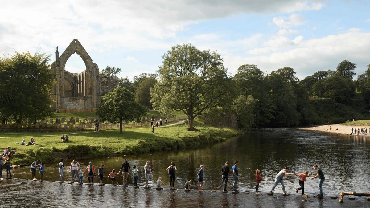 People using stepping stones to cross the River Wharfe at Bolton Abbey near Skipton, on the edge of the Yorkshire Dales National park in northern England on Bank Holiday, as many people opt to holiday at home rather than risk having to self-isolate for two weeks on return from a foreign holiday. Photo: AFP