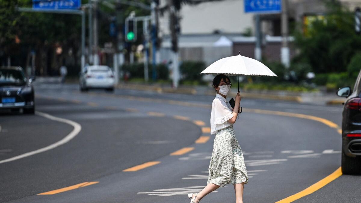 A pedestrian crossing a road while holding an umbrella to shelter from the sun amid record high temperatures in Shanghai. — AFP file