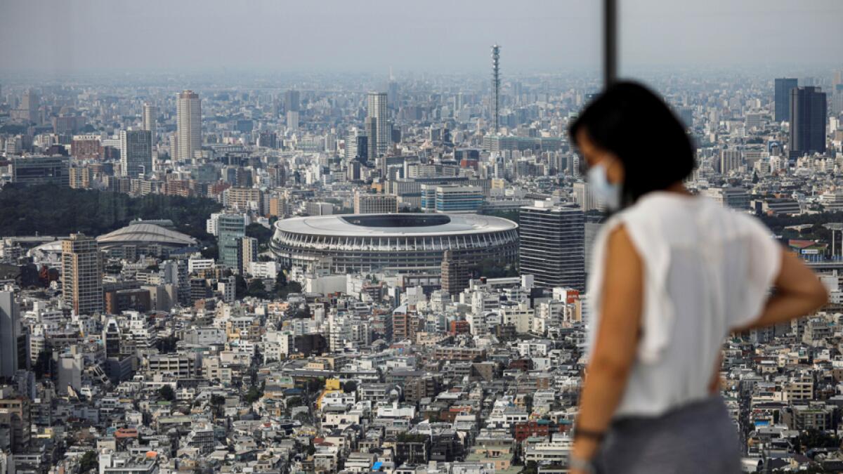 The National Stadium, the main stadium of Tokyo 2020 Olympics and Paralympics, is seen past a visitor wearing a protective face mask amid the coronavirus disease at an observation deck in Tokyo, Japan. Photo: Reuters