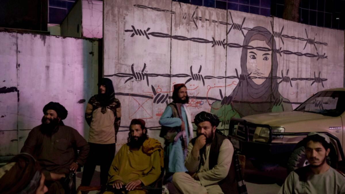 Taliban members sit in front of a mural depicting a woman behind barbed wire in Kabul. — AP