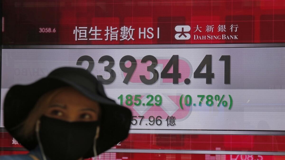 A woman wearing a face mask walks past an electronic board showing Hong Kong share index outside a local bank in Hong Kong, on Tuesday. Asian shares are rising, echoing the rally on Wall Street fuelled by signs of hope that the coronavirus pandemic could be slowing. - AP