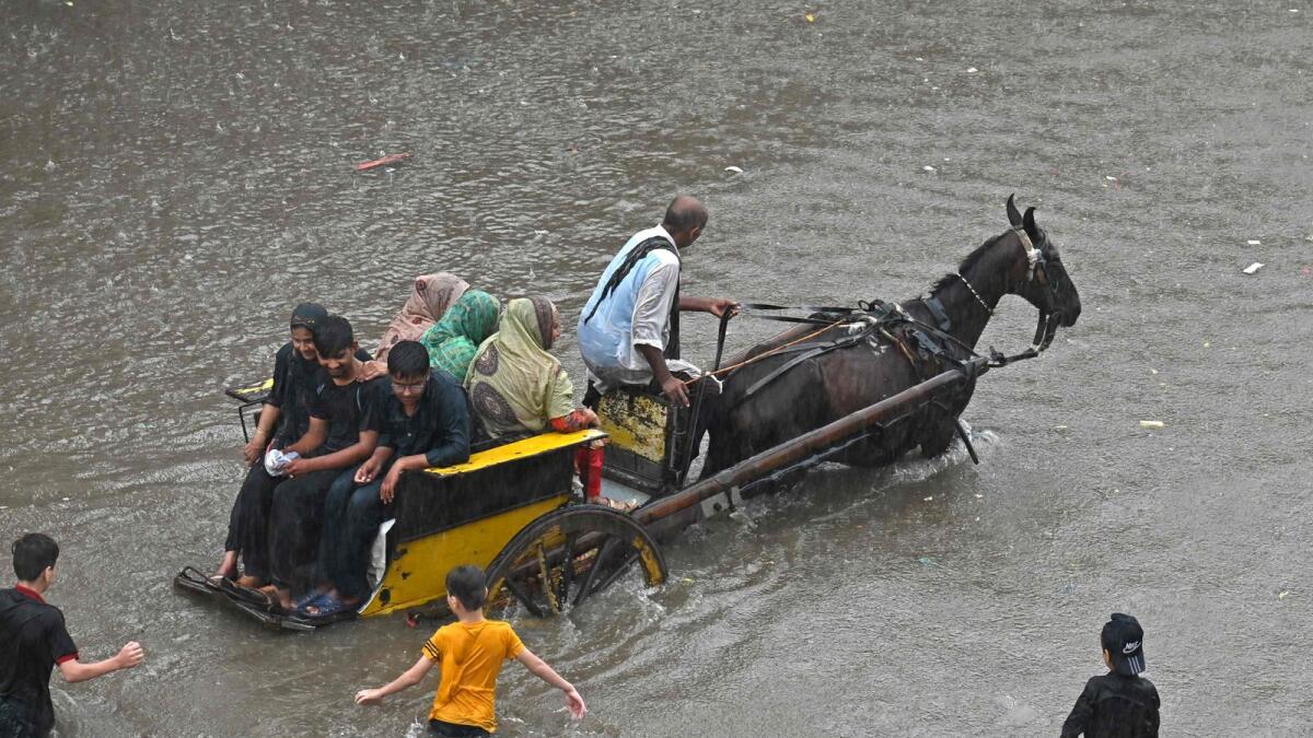 People ride on a horsecart through a flooded street after heavy rainfall in Lahore on July 5. — AFP