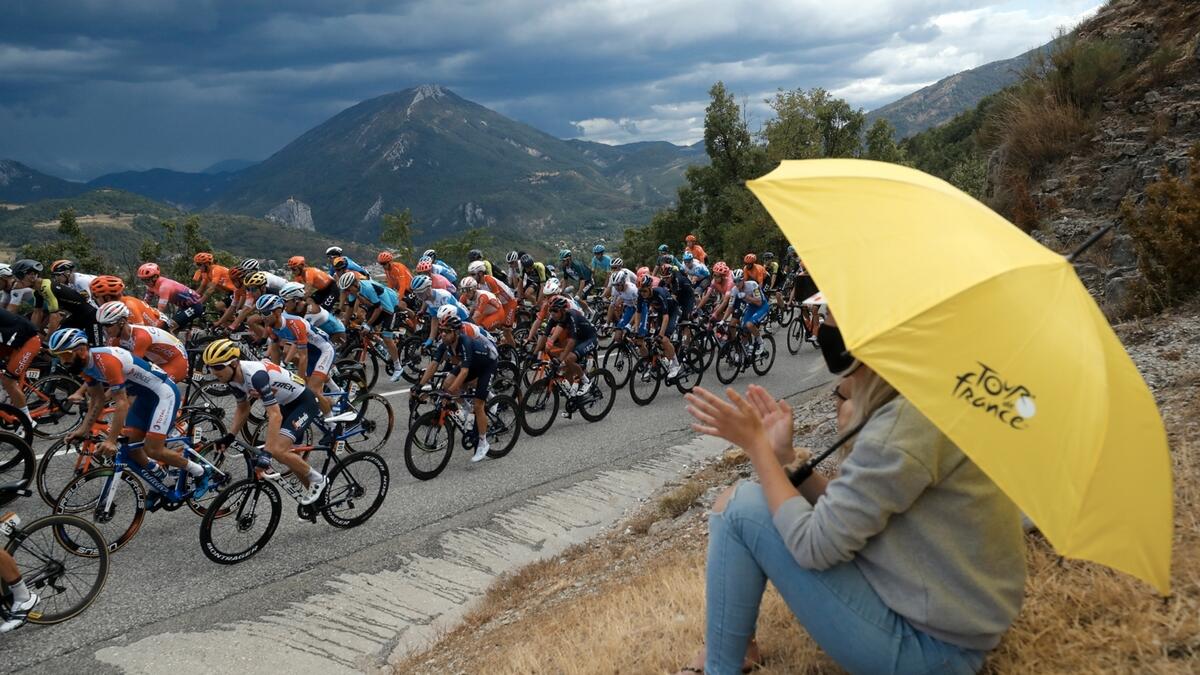A woman carries a yellow umbrella with the Tour de France logo as the peloton passes by in France. Photo: Reuters