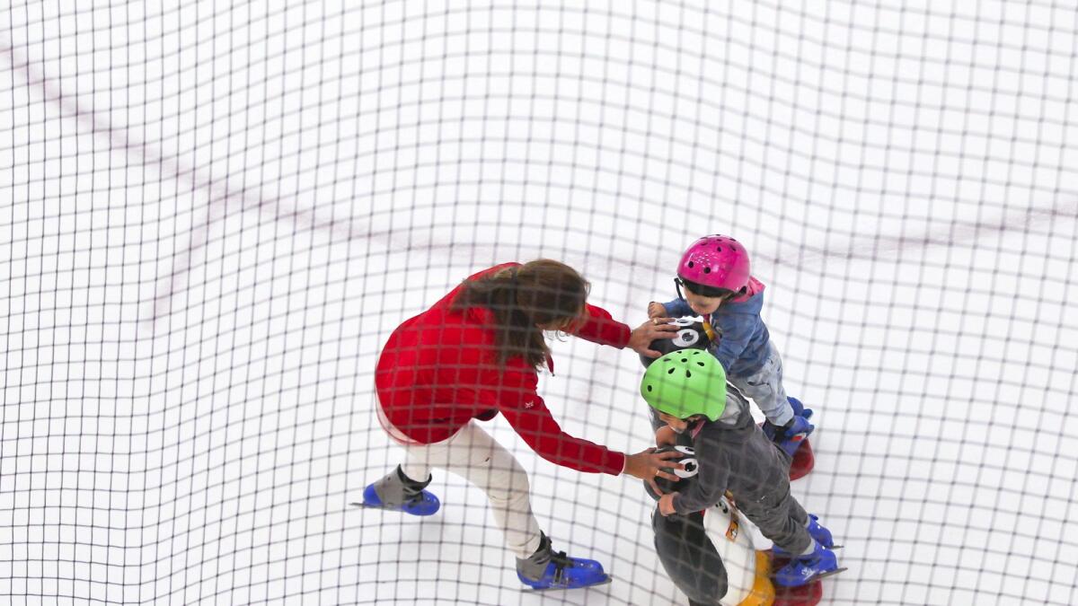 A lady helps two kids skate at the Dubai Mall.