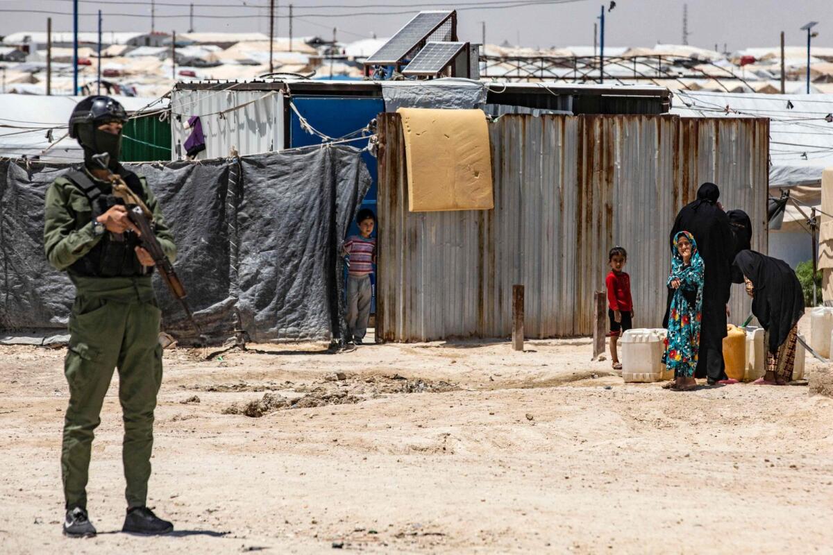 A member of Kurdish security forces stands guard as women and children fill water containers at the Al Hol camp in Syria's northeastern Al Hasakah Governorate, on October 10, 2023. — AFP