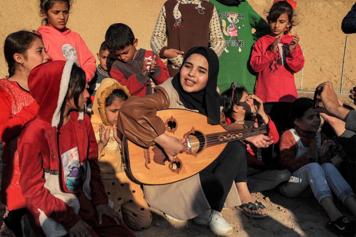 Ruaa Hassouna plays music for Palestinian children on her Oud (Ud, or oriental lute) as Palestinian children participate in an activity aimed to support their mental health, amid continuing battles between Israel and the militant group Hamas in Rafah in the southern Gaza Strip on on December 18, 2023.  — AFP