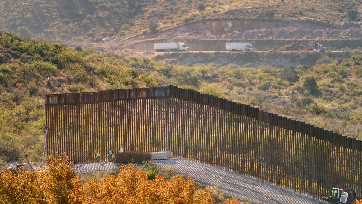 Trucks drive along Mexico’s Route 2, top, as border wall construction continues along a cleared pathway, on Dec. 9, 2020, in Guadalupe Canyon, Arizona.