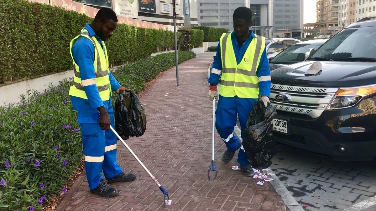 Richard and Joseph at work, filling trash bags with massage cards strewn on a street in Barsha Heights.