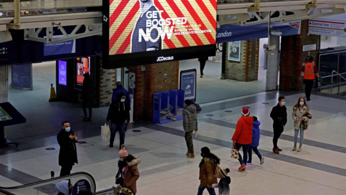 Pedestrians, some wearing face coverings to combat the spread of Covid-19, walk past a screen displaying a government advertisement promoting the NHS vaccine Booster programme, at Liverpool Street train station in central London. — AFP