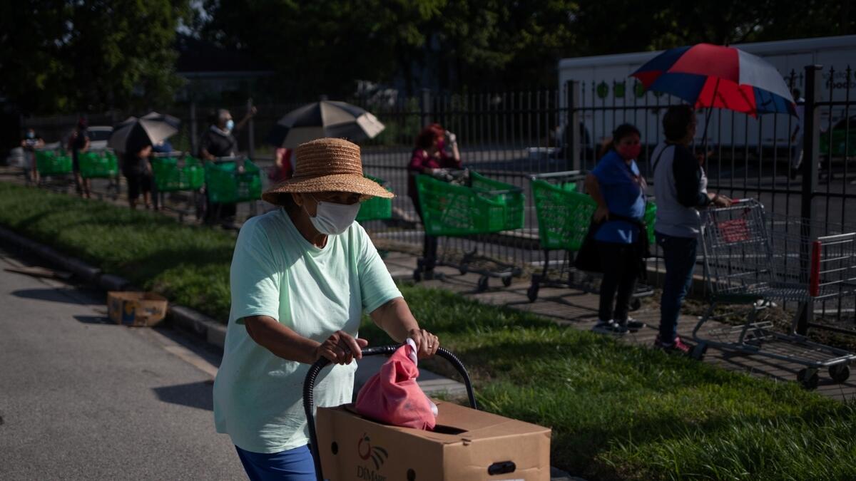 Others await in the background as a woman pushes a cart with groceries she received from the Wesley Community Center which were distributed to residents affected by the economic fallout from the coronavirus disease (COVID-19) outbreak in Houston, Texas, U