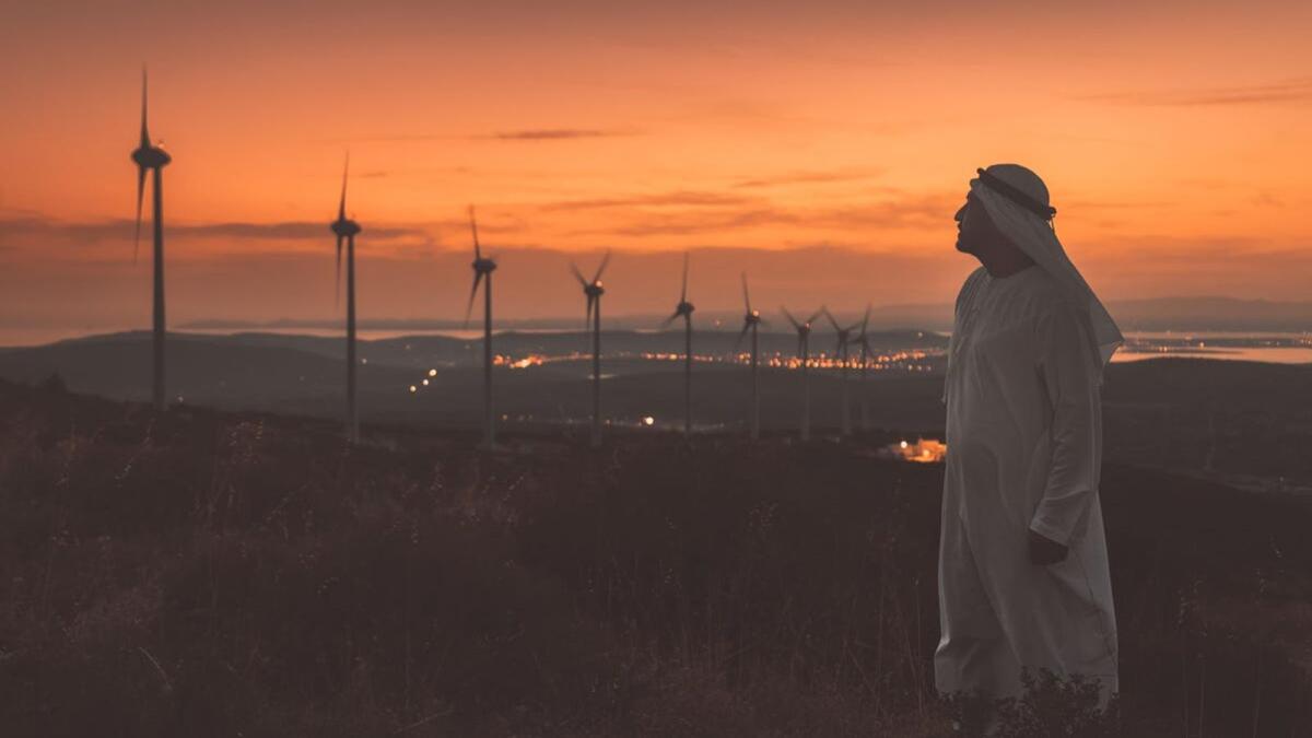 A man in traditional Emirati clothing looks at a row of wind turbines at sunset. Analysts at the World Economic Forum have warned that developing countries will be hit harder by climate change.