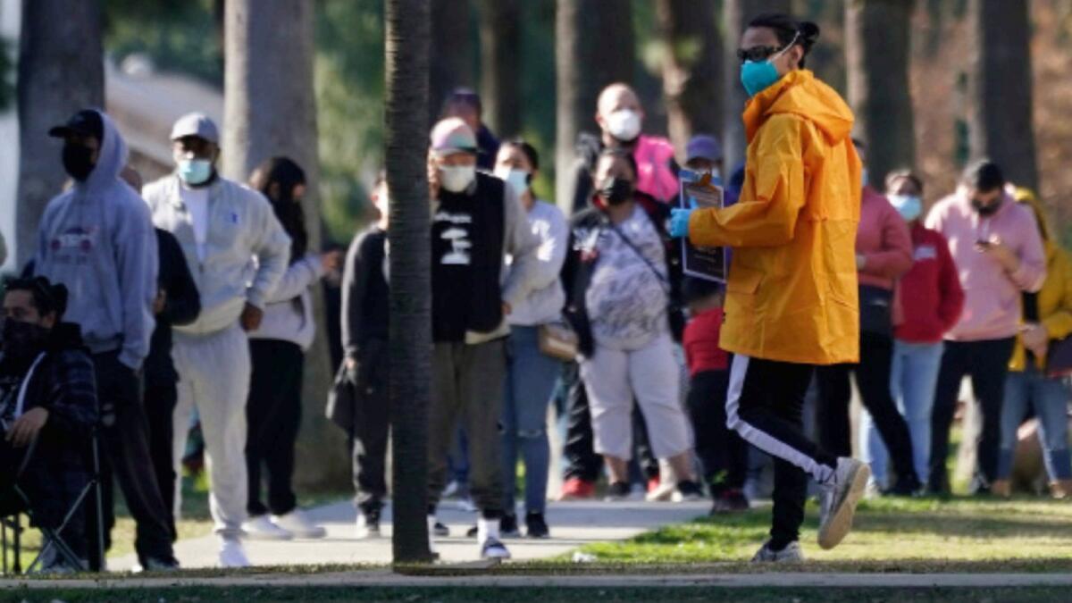 A man helping to facilitate tests for Covid-19 walks toward people waiting in line for tests in Long Beach California. — AP