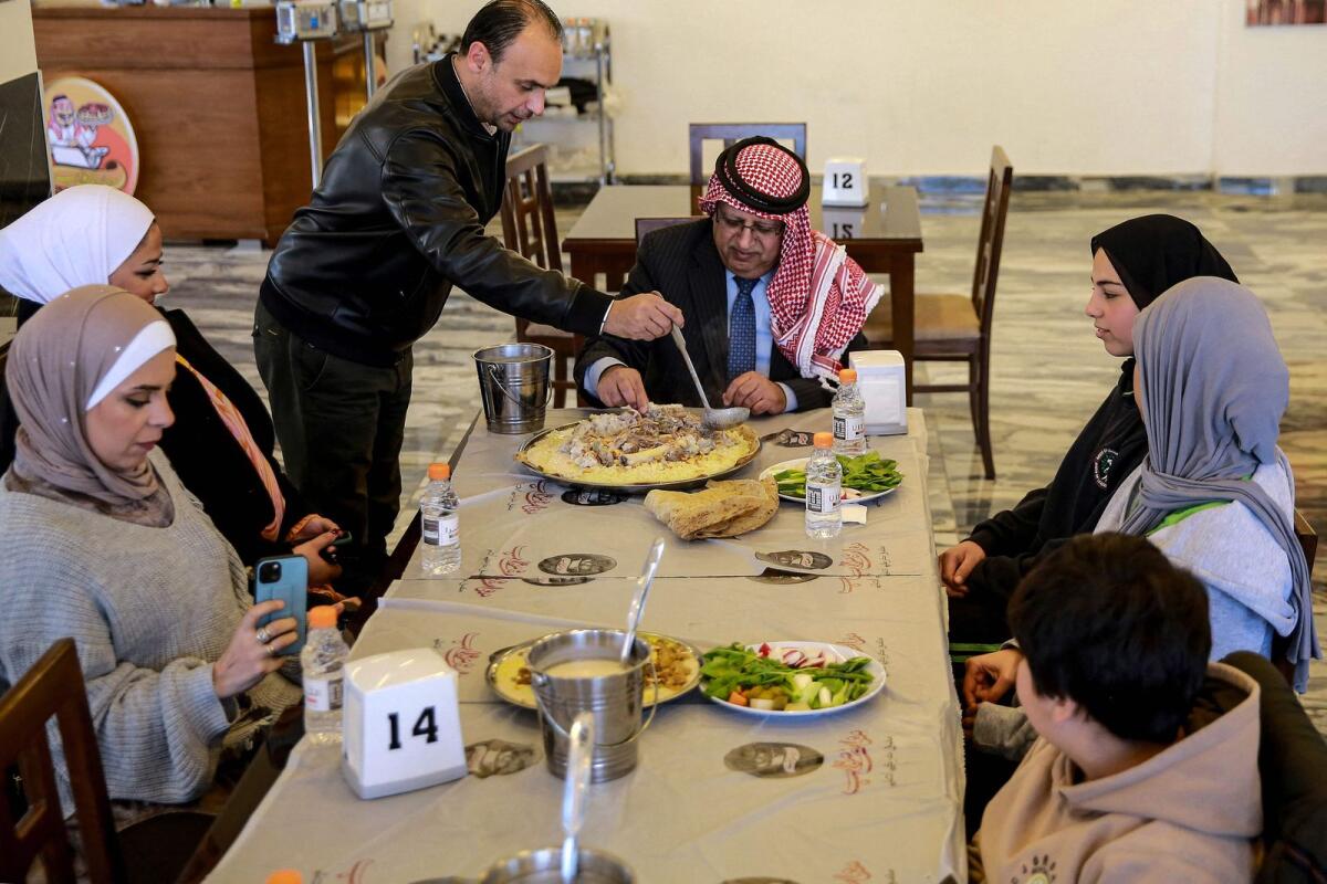 Tamer Majal (C-L), co-owner of a traditional restaurant, serves a dish of 'Mansaf' to Jordanian writer and researcher Hasan Mubaydin (C) and other patrons at his restaurant in Amman on March 16, 2023.  — AFP