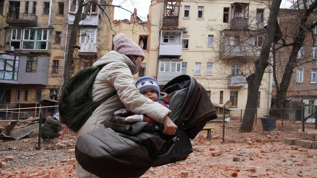 A woman carries her child as they evacuate from a residential building which was hit by a Russian rocket at the city center of Kharkiv, Ukraine, on Monday. — AP