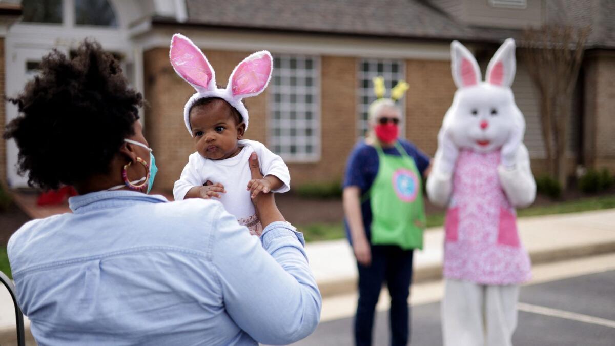 A woman holds her baby as they approach a person dressed as an Easter Bunny during an Easter event in Alexandria, Virginia. Photo: AFP