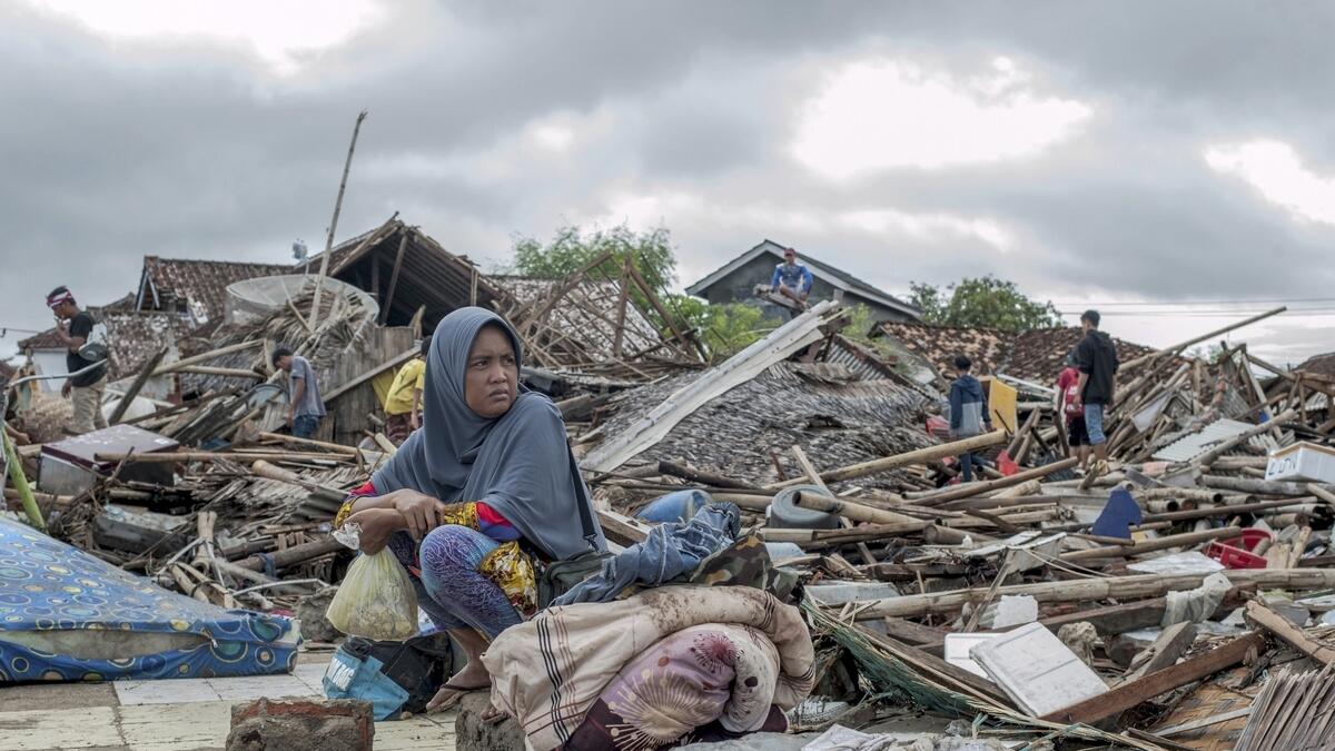 A tsunami survivor sits on a piece of debris as she salvages items from the location of her house in Sumur, Indonesia.. — AP file