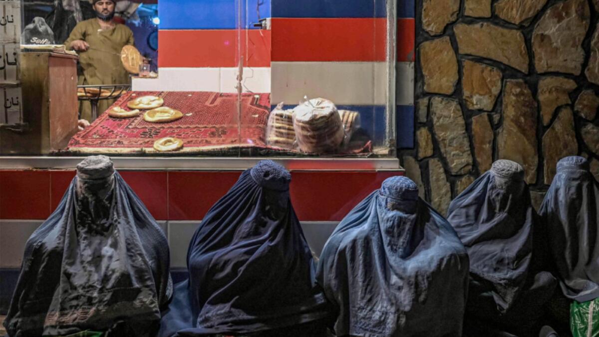 Burqa-clad women sit in front of a bakery as they seek alms in Kabul. — AFP