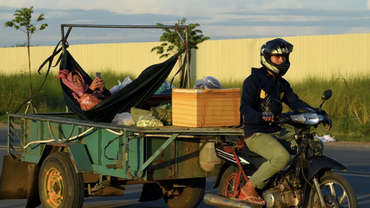 A man rides a motorbike pulling a trailer with a woman relaxing in a hammock, checking her phone, on a street in Phnom Penh on June 12, 2020. Photo: AFP
