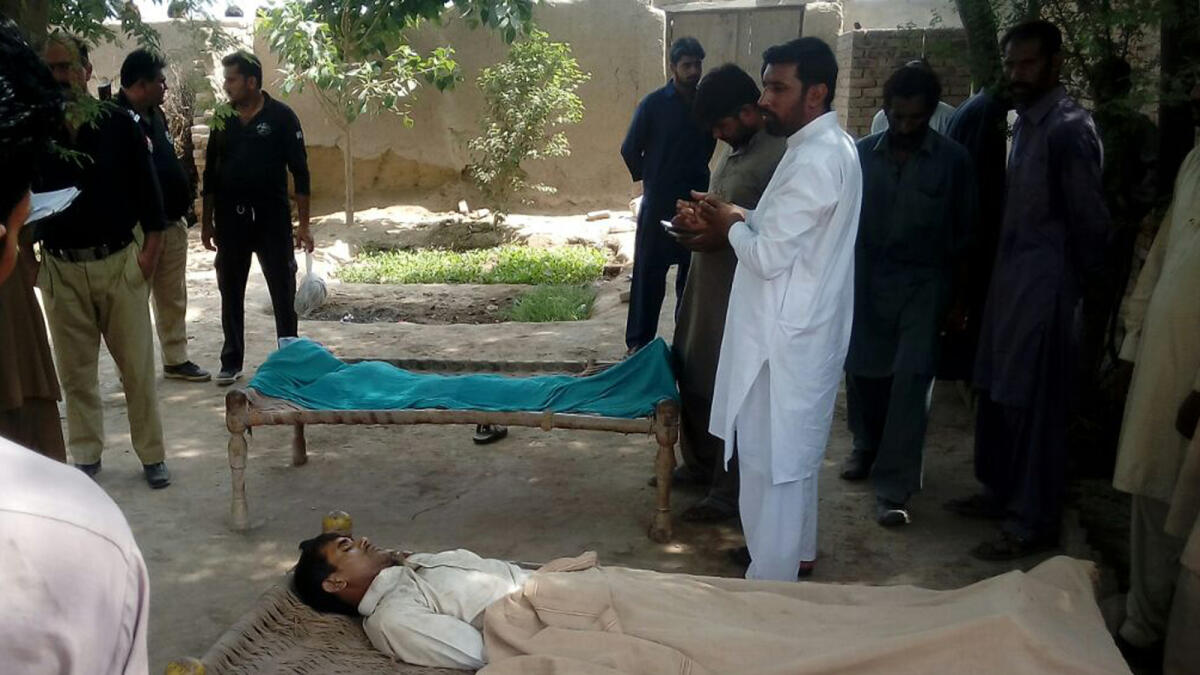 Police officials stand near the bodies of a woman and her alleged paramour who were hanged to death by the woman’s father, brother and husband in a village in Multan. 
