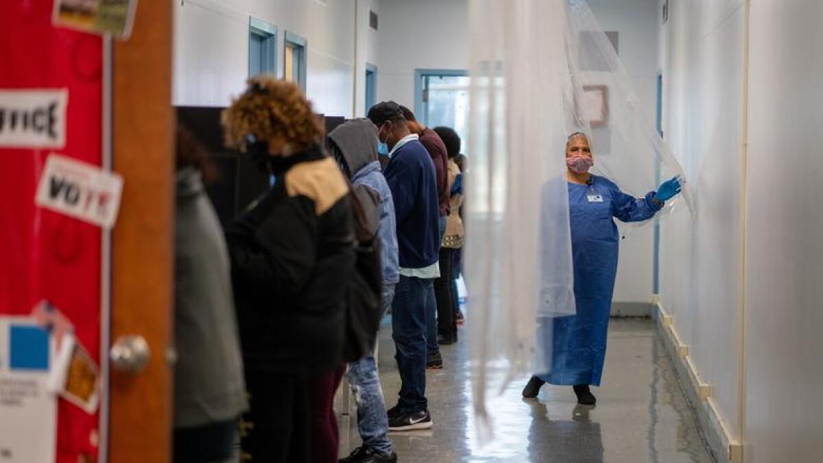 A poll worker walks past people cast their votes for the upcoming presidential election as early voting begins in New Orleans, Louisiana