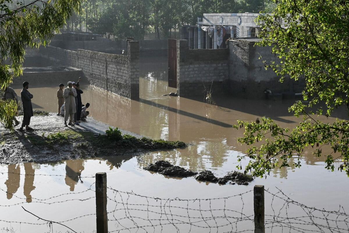 Residents stand near the flooded waters outside their homes following heavy rains in Charsadda district of Khyber Pakhtunkhwa province on Wednesday. — AFP