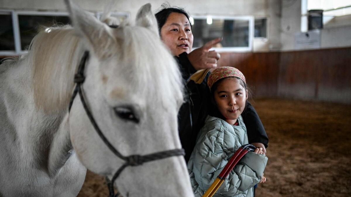 This picture taken on February 28, 2023 shows a young girl with autism spectrum disorder looking at her horse before a riding lesson at a horse club in Beijing. _ AFP