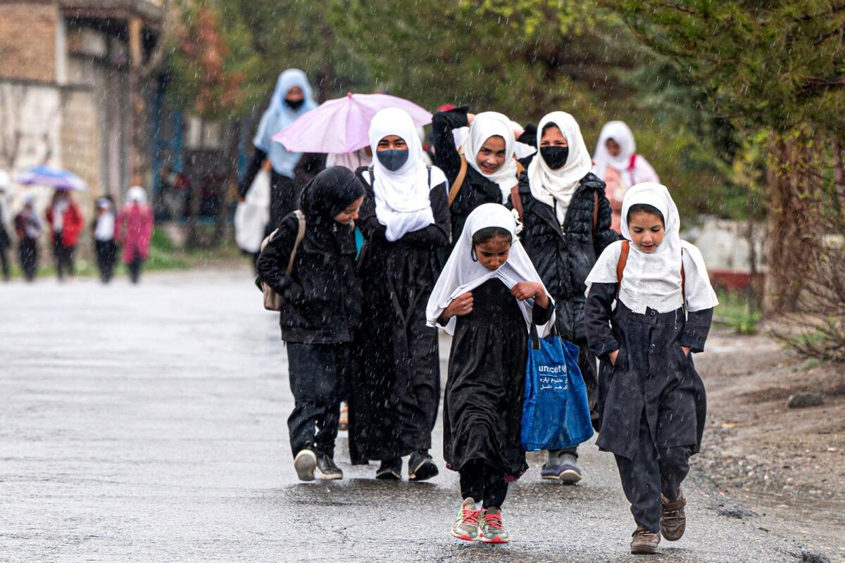 Afghan school girls walk amid rainfall along a road in Paghman district on the outskirts of Kabul on March 30, 2023. — AFP