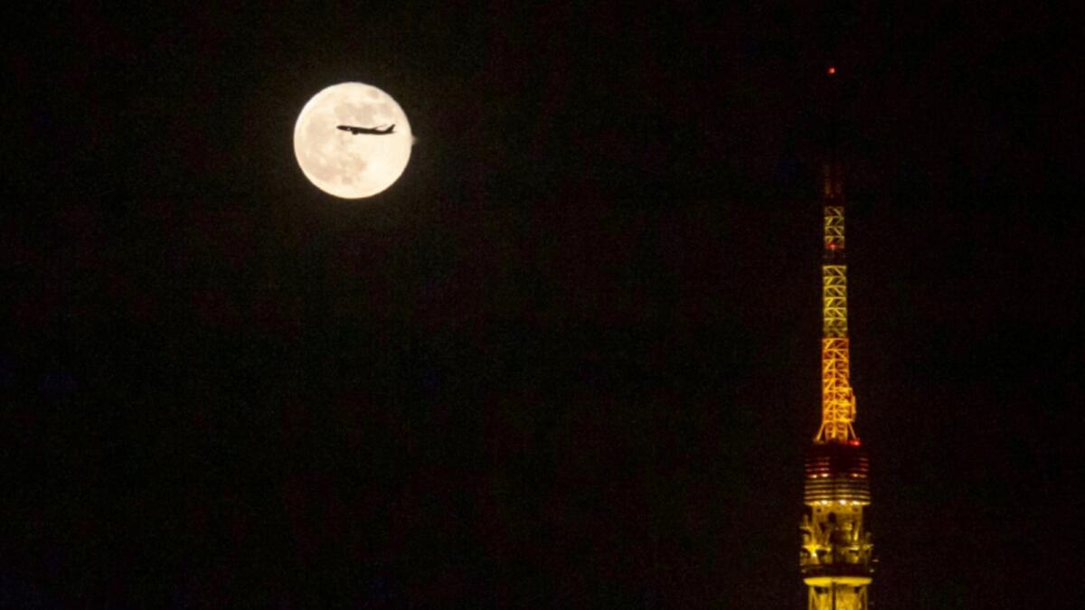 An airplane flies past the moon rising over Tokyo Tower. — AP