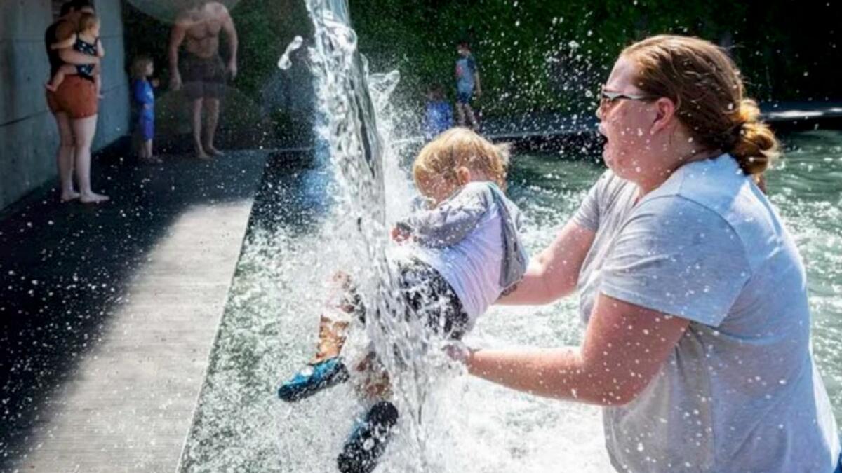 A woman holds a young child under a waterfall at a park in Washington, DC, on June 28, 2021, as a heatwave moves over much of the US. Photo: AFP